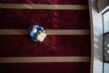 Image showing muslim man praying Allah alone inside the mosque and reading islamic holly book