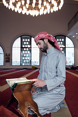 Image showing muslim man praying Allah alone inside the mosque and reading islamic holly book