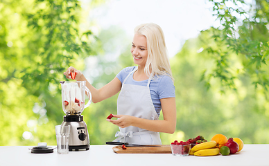 Image showing smiling woman with blender making fruit smoothie