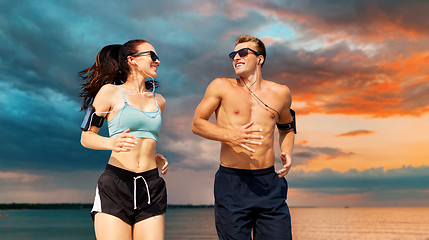 Image showing couple with phones and arm bands running over sea