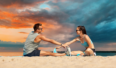 Image showing smiling couple stretching legs on beach