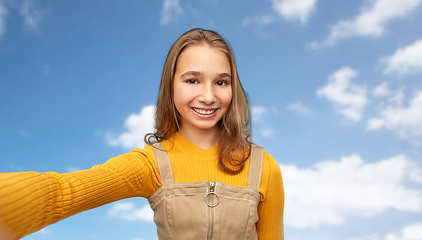 Image showing happy teenage girl taking selfie over sky