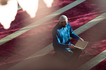 Image showing muslim man praying Allah alone inside the mosque and reading islamic holly book