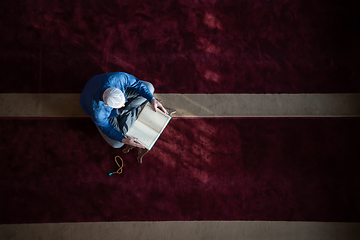 Image showing muslim man praying Allah alone inside the mosque and reading islamic holly book