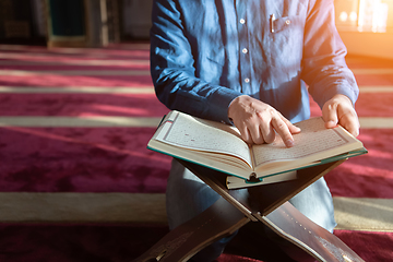 Image showing muslim man praying Allah alone inside the mosque and reading islamic holly book