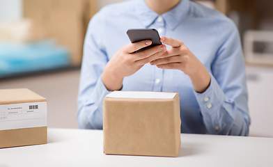 Image showing woman with smartphone and parcels at post office