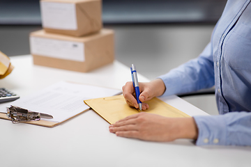 Image showing woman writing on parcel envelope at post office