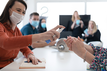 Image showing new normal businesspeople on meeting using antibacterial hand sanitizer