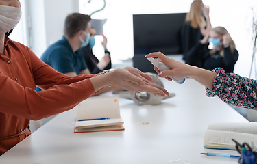 Image showing new normal businesspeople on meeting using antibacterial hand sanitizer