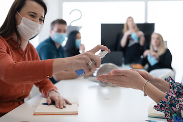 Image showing new normal businesspeople on meeting using antibacterial hand sanitizer