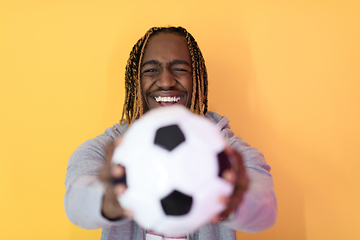 Image showing afro man posing on a yellow background while holding a soccer ball