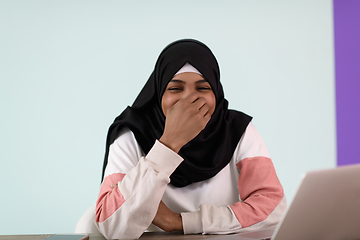 Image showing afro muslim woman wearing a hijab sits smiling in her home office and uses a laptop