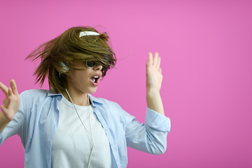 Image showing brunette lady in black glasses dancing and listening music isolate on pink background