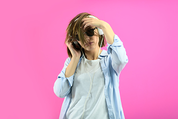 Image showing brunette lady in black glasses dancing and listening music isolate on pink background