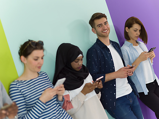 Image showing diverse teenagers use mobile devices while posing for a studio photo in front of a pink background