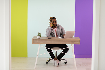 Image showing afro young man sits in his home office during a pandemic and uses the phone