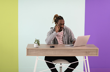 Image showing afro young man sits in his home office during a pandemic and uses the phone