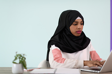 Image showing afro girl wearing a hijab thoughtfully sits in her home office and uses a laptop