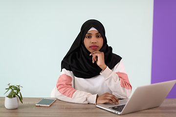 Image showing afro girl wearing a hijab thoughtfully sits in her home office and uses a laptop