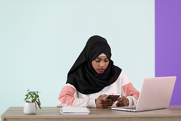 Image showing afro girl wearing a hijab thoughtfully sits in her home office and uses a laptop