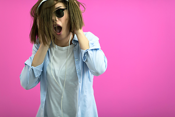 Image showing brunette lady in black glasses dancing and listening music isolate on pink background