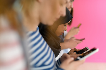 Image showing diverse teenagers use mobile devices while posing for a studio photo in front of a pink background