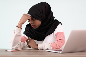 Image showing afro girl wearing a hijab is disappointed and sad sitting in her home office and using a laptop