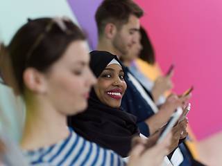 Image showing diverse teenagers use mobile devices while posing for a studio photo in front of a pink background