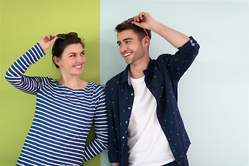 Image showing Beautiful young loving couple adjusting their sunglasses while standing against green-grey background