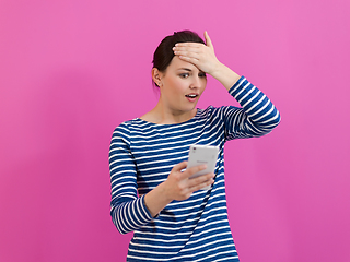 Image showing isappointed-faced girl looks at her cell phone as she stands in front of a pink background