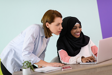 Image showing afro muslim woman wearing a hijab sits smiling in her home office and using laptop for online meeting