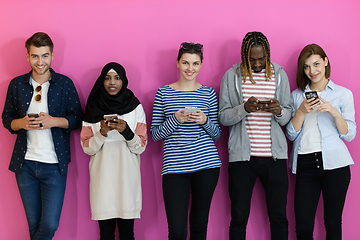 Image showing diverse teenagers use mobile devices while posing for a studio photo in front of a pink background