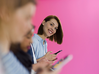 Image showing diverse teenagers use mobile devices while posing for a studio photo in front of a pink background