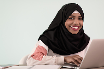 Image showing afro muslim woman wearing a hijab sits smiling in her home office and uses a laptop