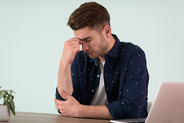 Image showing disappointed and annoyed man sitting at a table and looking at a laptop