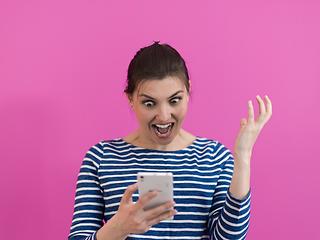 Image showing surprised-faced girl looks at her cell phone as she stands in front of a pink background