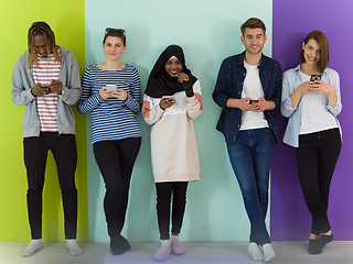 Image showing diverse teenagers use mobile devices while posing for a studio photo in front of a pink background