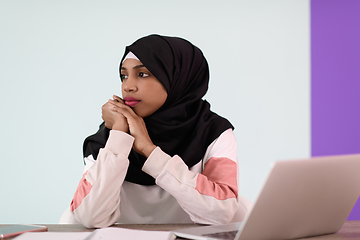 Image showing afro girl wearing a hijab thoughtfully sits in her home office and uses a laptop