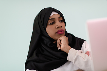 Image showing afro girl wearing a hijab thoughtfully sits in her home office and uses a laptop