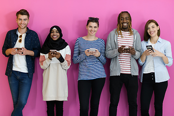 Image showing diverse teenagers use mobile devices while posing for a studio photo in front of a pink background