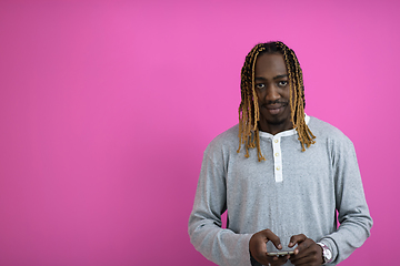 Image showing afro guy uses a phone while posing in front of a pink background.