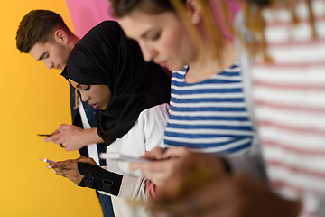 Image showing diverse teenagers use mobile devices while posing for a studio photo in front of a pink background