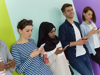 Image showing diverse teenagers use mobile devices while posing for a studio photo in front of a pink background