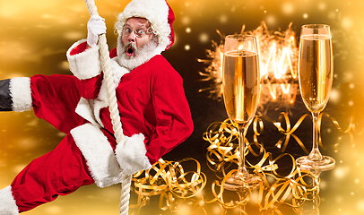 Image showing Happy Christmas Santa Claus climbing on rope with glasses of champagne in background