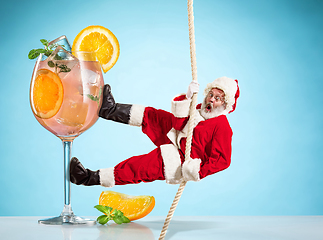 Image showing Happy Christmas Santa Claus climbing on rope on blue background