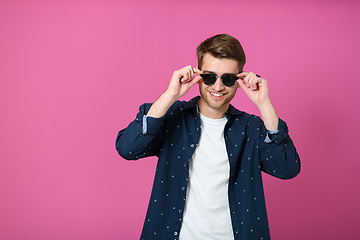 Image showing a portrait of a young man wearing a blue shirt and posing in front of a pink background 