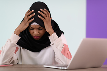 Image showing afro girl wearing a hijab is disappointed and sad sitting in her home office and using a laptop