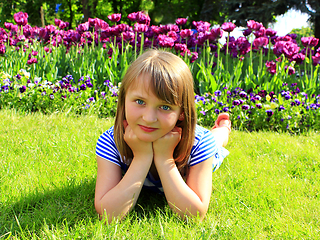 Image showing school girl lays on the grass and besides tulips