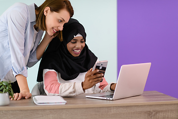 Image showing afro girl with a hijab and a European woman use a cell phone and laptop in their home office