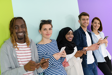 Image showing diverse teenagers use mobile devices while posing for a studio photo in front of a pink background